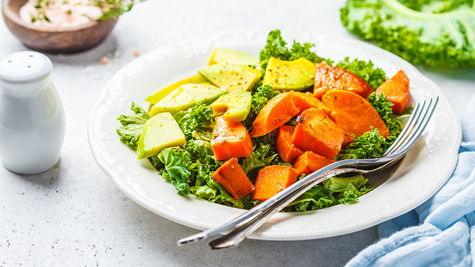 kale salad with sweet potatoes and avocado on a white plate